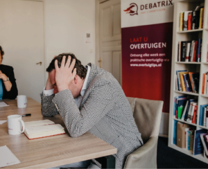 meneer met jasje doet handen op zijn hoofd bij een vergadering